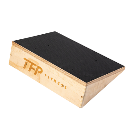 A wooden slant board with a black textured top surface and natural wood sides, featuring the 'TFP FITNESS' logo printed on the side, shown on a plain white background.